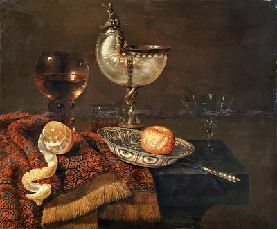A clementine in a porcelain bowl, a nautilus cup, a roemer, two glasses, a knife, a peeled lemon on an ornamental carpet on…