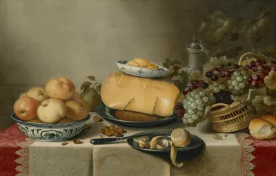 Cheese and a butter dish on a pewter plate, apples in a porcelain bowl, a basket of grapes, and a partially peeled lemon on…